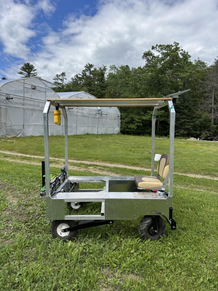 A photo of the robotic tractor in front of greenhouses