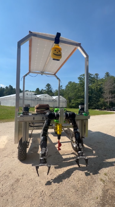 A photo of a robotic tractor in front of greenhouses